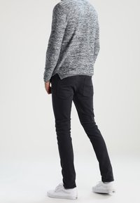 Dunkle, enganliegende Jeans mit fünf Taschen, getragen mit einem grauen, strukturierten Pullover. Weiße Sneakers vervollständigen das lässige Outfit.
