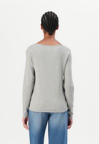 Light gray long-sleeve shirt made of soft fabric, featuring a scoop neckline and a relaxed fit, paired with blue denim jeans.