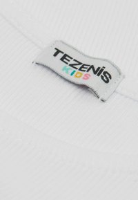 Bílá �žebrovaná tkanina s štítkem „TEZENIS KIDS“ v černých a barevných písmenech, která ukazuje hladký povrch a zaoblené hrany.