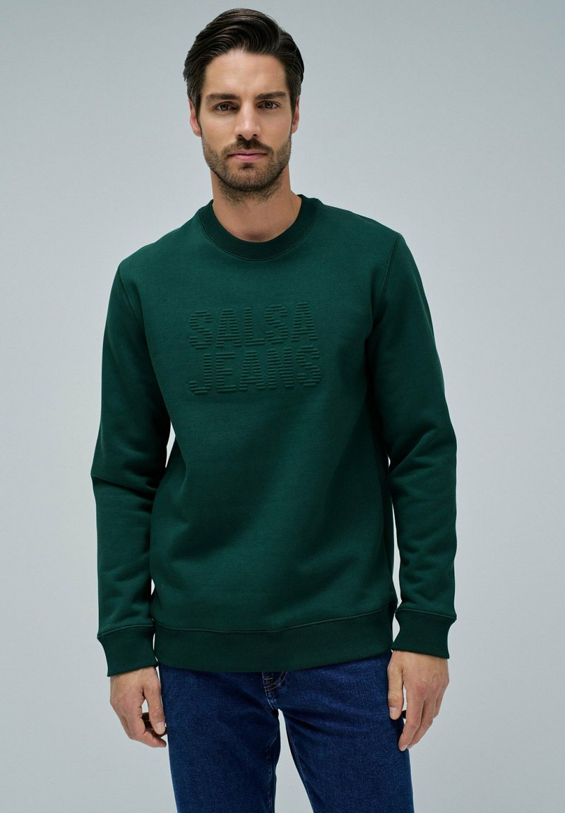 Felpa verde con colletto tondo e maniche lunghe. Presenta la scritta rialzata "SALSA JEANS" sulla parte anteriore. Realizzata in materiale morbido e liscio.