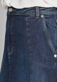 Jupe en denim bleu foncé avec une taille haute, fermeture par bouton à rivet et surpiqûres jaunes mettant en valeur les coutures et les poches.