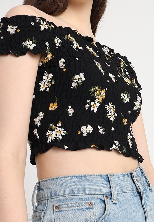 Černý, bezramenní, zkrácený top s texturovanou tkaninou. Má malé, multikulturní květinové vzory a volánový okraj. Spárovaný s světlým denimem.