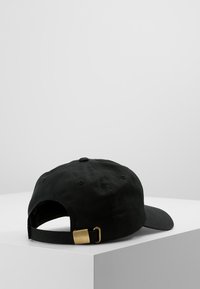 Cappellino da baseball in cotone nero con visiera curva, fascia regolabile con fibbia in metallo dorato e fori di ventilazione cuciti.