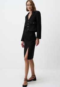 Ensemble noir texturé en deux pièces comprenant un blazer court avec une poche unique et une fermeture à bouton, associé à une jupe longueur genou avec une fente sur le côté.