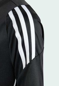 Čierna športová bunda s rúčkom a tromi bielymi pruhmi, vyrobená z hladkej textílie a s priliehavým strihom. Bočný šev vykazuje miernu variáciu textúry.
