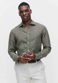 Olijfgroene linnen shirt met een button-down kraag, een voorpand met knopen en mouwen met manchetten, gecombineerd met lichtbeige broeken en een gevlochten riem.