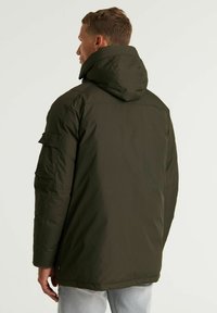 Chaqueta acolchada verde oscuro con capucha, con cierre de cremallera y bolsillos laterales. Textura suave y corte relajado, diseñada para mantener el calor.