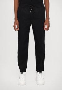Black sweatpants with an elastic drawstring waistband, tapered legs, and cuffs. Paired with white sneakers for contrast.