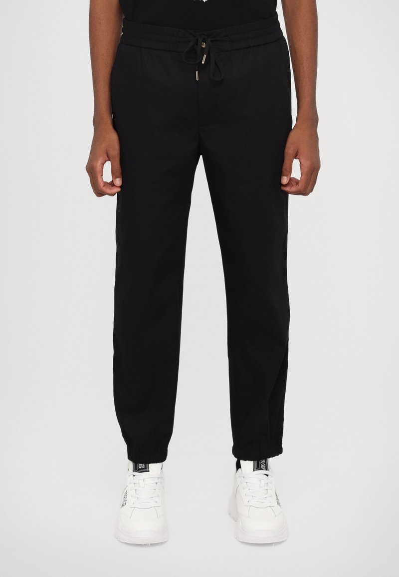 Black sweatpants with an elastic drawstring waistband, tapered legs, and cuffs. Paired with white sneakers for contrast.