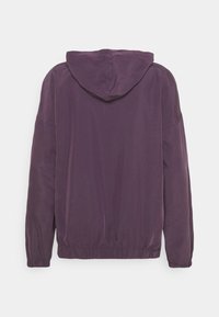 Fialová lehká bunda s kapucí, elastickými manžetami a spodním lemem. Hladká textura s minimem detailů a volným střihem.