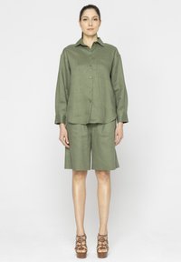 Oliwkowa lniana koszula z długim rękawem i kołnierzykiem, połączona z dopasowanymi szortami. Brązowe, zapięte na paski platformy zwieńczają tę stylizację.
