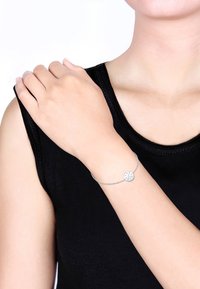 Silver kedjearmband med en cirkulär berlock med minimalistisk design och graverade detaljer, bärs på en bar handled.