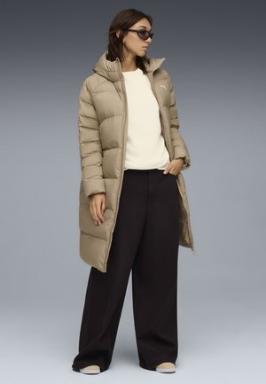 Beige pufferjas met een hoge kraag, lange lengte en doorgestikt textuur. Draag het over een lichte trui en gecombineerd met wijde zwarte broek en sneakers.