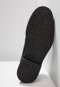 Fekete cipőtalp, amely texturált profilt mutat be. Tartós gumimaterial, a szélén kiemelkedő logóval. Enyhén ívelt forma.