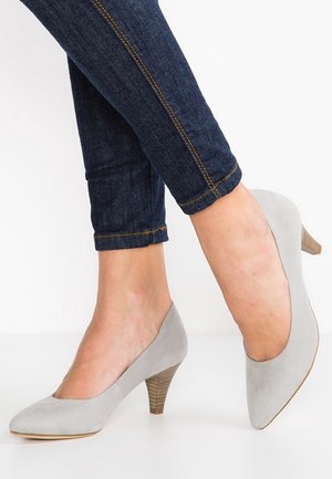 Escarpin en daim gris avec un bout arrondi et un talon en bois de hauteur intermédiaire, associé à un jean en denim foncé avec un ourlet roulé et des coutures contrastantes.