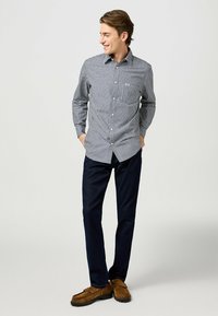 Camicia a righe bianca e nera con taschino, abbinata a pantaloni blu scuro e mocassini in suede marrone.