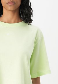 Gai zaļš kokvilnas t-krekls ar īsām piedurknēm, apaļu kaklu un mazu sudraba Nike logo uz krūšu. Gluda tekstūra, brīvs piegriezums.