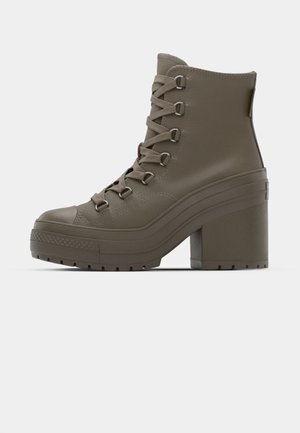 Botas de canos baixos em caqui com um tacão alto em bloco, sola de borracha texturada, atacadores proeminentes e fabricadas em material sintético liso.