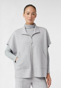 Giacca leggera grigia con zip e maniche corte, realizzata in tessuto morbido. Presenta un colletto alto e tasche frontali. Maniche con texture.