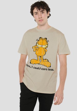 Beige cotton t-shirt featuring an orange cartoon cat graphic and text that says “Yes, I could care less.” Short sleeves and relaxed fit.