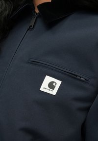 Ναυτικό μπλε μπουφάν με φερμουάρ, διαθέτει μαύρο βελούδινο γιακά, τσέπη στο στήθος και λευκό τετράγωνο λογότυπο στην α ριστερή πλευρά.