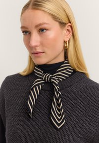 Silk neck scarf with navy and cream diagonal stripes, tied around the neck, paired with a dark textured sweater.