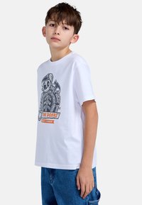 Weißes Baumwoll-T-Shirt mit einem schwarzen Grafikbild eines Skeletts mit Werkzeugen und dem Text "THE DOERS" in Orange. Mit kurzen Ärmeln und Rundhalsausschnitt.