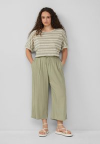 Lichtgroene gestreepte top met korte mouwen, luchtige lichtgroene broek met elastische tailleband en off-white sandaaltjes met bandjes.