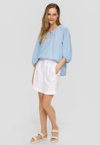 Himmelbluse mit Streifen, Ballonärmeln und Schlüssel-Ausschnitt, kombiniert mit weißen Leinen-Shorts und hellbeigen Plateausandalen.