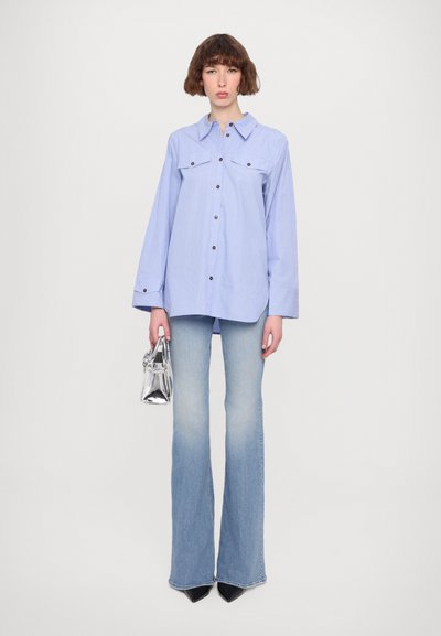 Camicia a righe blu chiaro con bottoni, dotata di due tasche sul petto, abbinata a jeans a zampa d'elefante sbiaditi e a una piccola borsa a tracolla argentata.