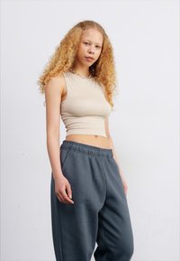 Top corto sin mangas color beige combinado con pantalones de chándal grises. El top presenta un diseño ajustado, y los pantalones de chándal son holgados con una cinturilla elástica.