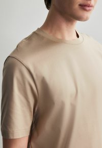 Beige bomulds t-shirt med rund halsudskæring, korte ærmer og glat tekstur. Designet er enkelt uden synlige mønstre eller accenter.