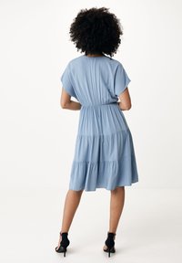 Světle modré šaty s krátkým rukávem, elastickým pasem a vrstevnatým volánkem na spodním lemu. Vyrobeno z hladkého materiálu, vhodné na volný čas.