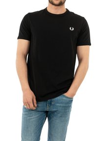 Camiseta de algodón negra con mangas cortas, cuello redondo y un pequeño logo blanco en el lado izquierdo del pecho. Combinada con jeans de mezclilla azul claro.