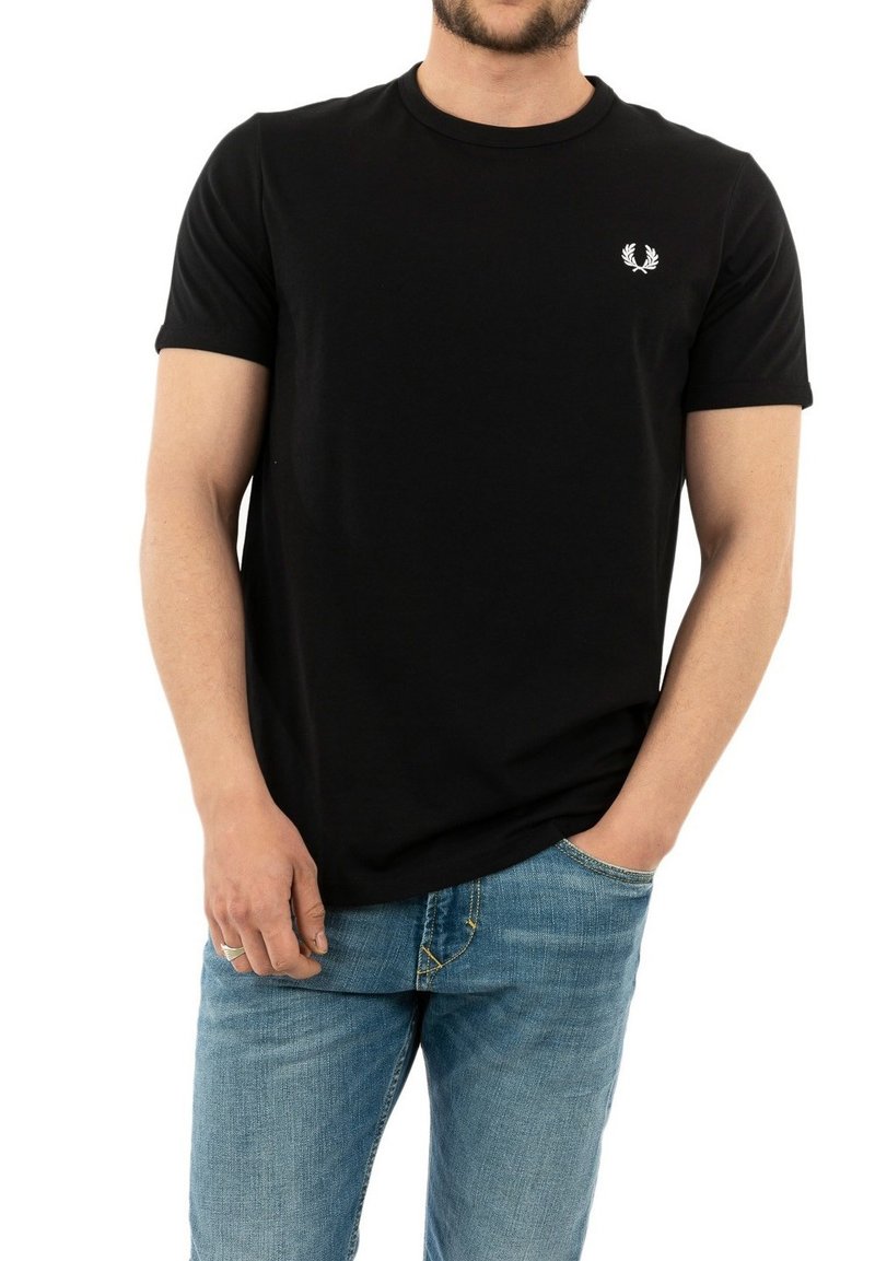 Camiseta de algodón negra con mangas cortas, cuello redondo y un pequeño logo blanco en el lado izquierdo del pecho. Combinada con jeans de mezclilla azul claro.