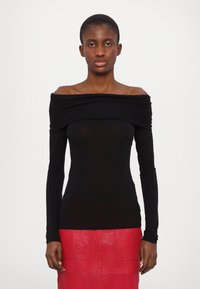 Zwarte off-the-shoulder top met lange mouwen en geplooid detail, gecombineerd met een gestructureerde, felrode rok. Gladde, aansluitende silhouet.