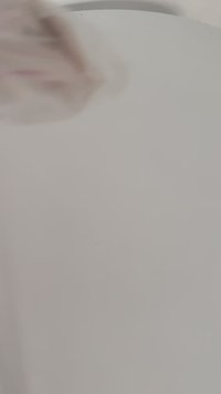 Campione di tessuto di colore chiaro con texture morbida, che mostra un leggero motivo. Un bordo sfocato indica movimento o interazione con il materiale.