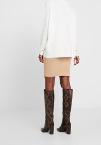 Bruine kniehoge laarzen met slangenprint, een gestructureerde afwerking en blokhak, gecombineerd met een aansluitende beige rok en een witte oversized trui.