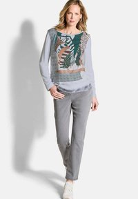 Langarmblouse met gemengde patronen, met strepen en dierenprints in groen, beige en grijs. Gecombineerd met grijze broek en witte sneakers.