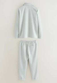 Vaaleanharmaa pitkähihainen poolopaita, jossa on kaulus, yhdistettynä samanvärisiin jogger-housuihin, joissa on joustava vyötärö ja resorit lahkeissa.