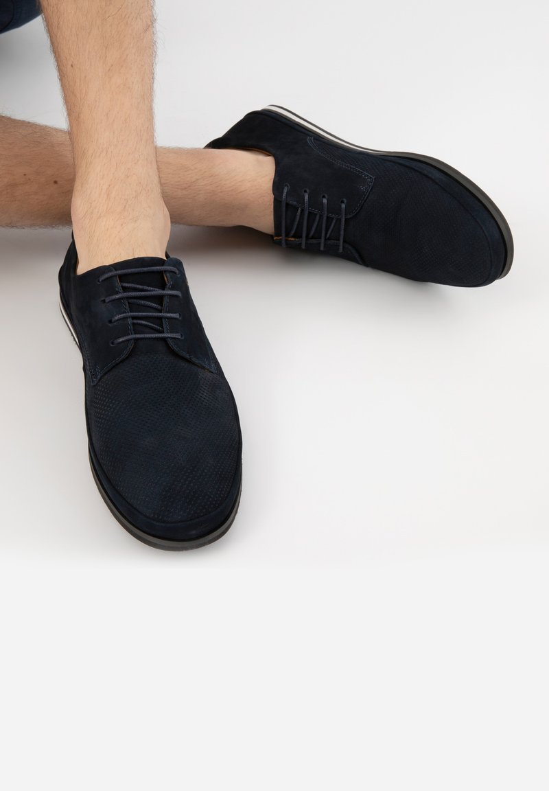 Navy semišové boty s texturovaným povrchem, s šněrovacím designem a kontrastní podrážkou. Viditelné švy dodávají detail modernímu tvaru.