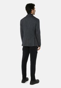 Textured grijze blazer met een klein ruitpatroon, enkele split en slim fit, gecombineerd met donkere broeken en zwarte schoenen.
