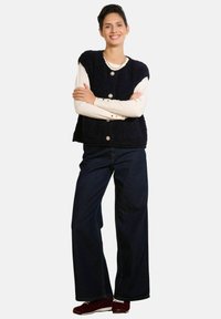 Tumši zils, pūkains vestes ar zelta pogām pārsvērts pār krēmkrāsas garām piedurknēm krekla. Kombinēts ar platu melnu džinsu bikšu un sarkaniem apaviem.