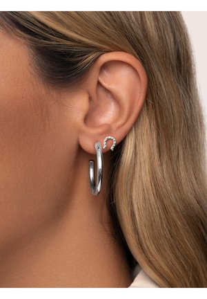 Pendientes de aros plateados y pequeños pendientes en forma de herradura, con un acabado brillante. El aro es grande, mientras que el pendiente de acento tiene piedras incrustadas.