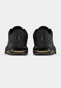 Černé sportovní boty s texturovaným materiálem, s výraznými logy Nike na patě a kontrastním zlatým akcentem na podrážce.