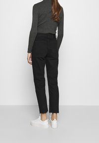 Jeans negros de cintura alta con corte recto, que presentan un dobladillo deshilachado y dos bolsillos en la parte posterior, combinados con zapatillas blancas.