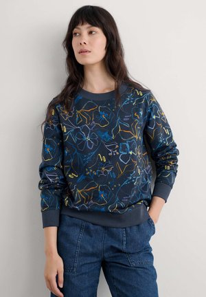 Sweatshirt marine avec des dessins floraux colorés en ligne. Il présente un col rond et des poignets côtelés, associé à un pantalon en denim.
