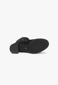 Stivaletto in suede nero con tacco spesso, dotato di zip laterale e suola in gomma liscia. Logo del marchio italiano stampato sulla suola.