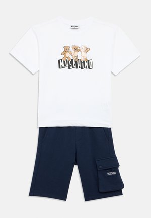Biały bawełniany t-shirt z trzema grafikami misiów i napisem „Moschino” poniżej. W zestawie granatowe szorty z boczną kieszenią.