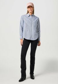 Randig blå och vit knapp-up skjorta, svarta jeans och en ljusrosa keps; har ficka, krage och figurnära design. Svarta ankelkängor.